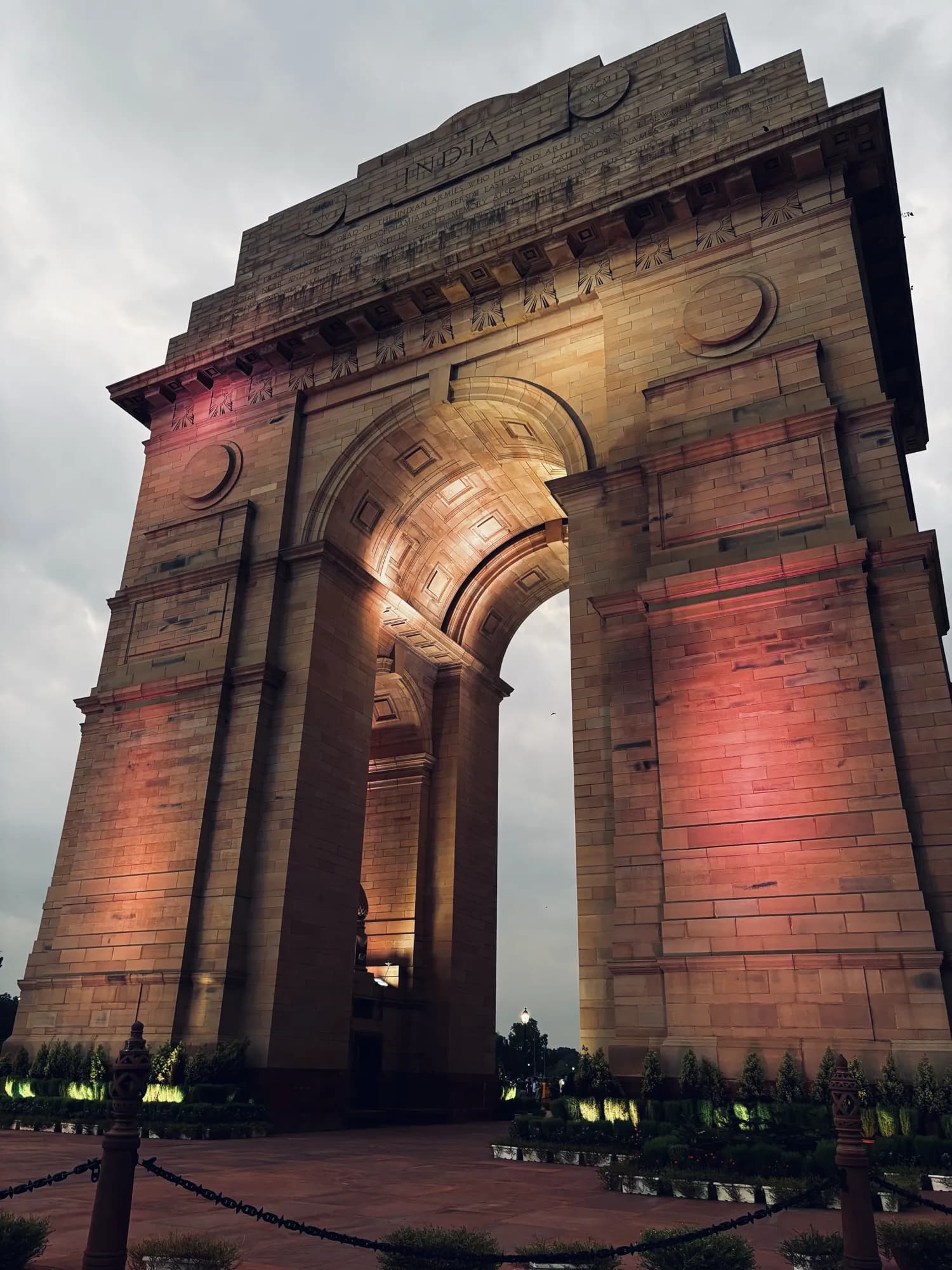 India Gate lit in warm pink and gold under a grey evening sky