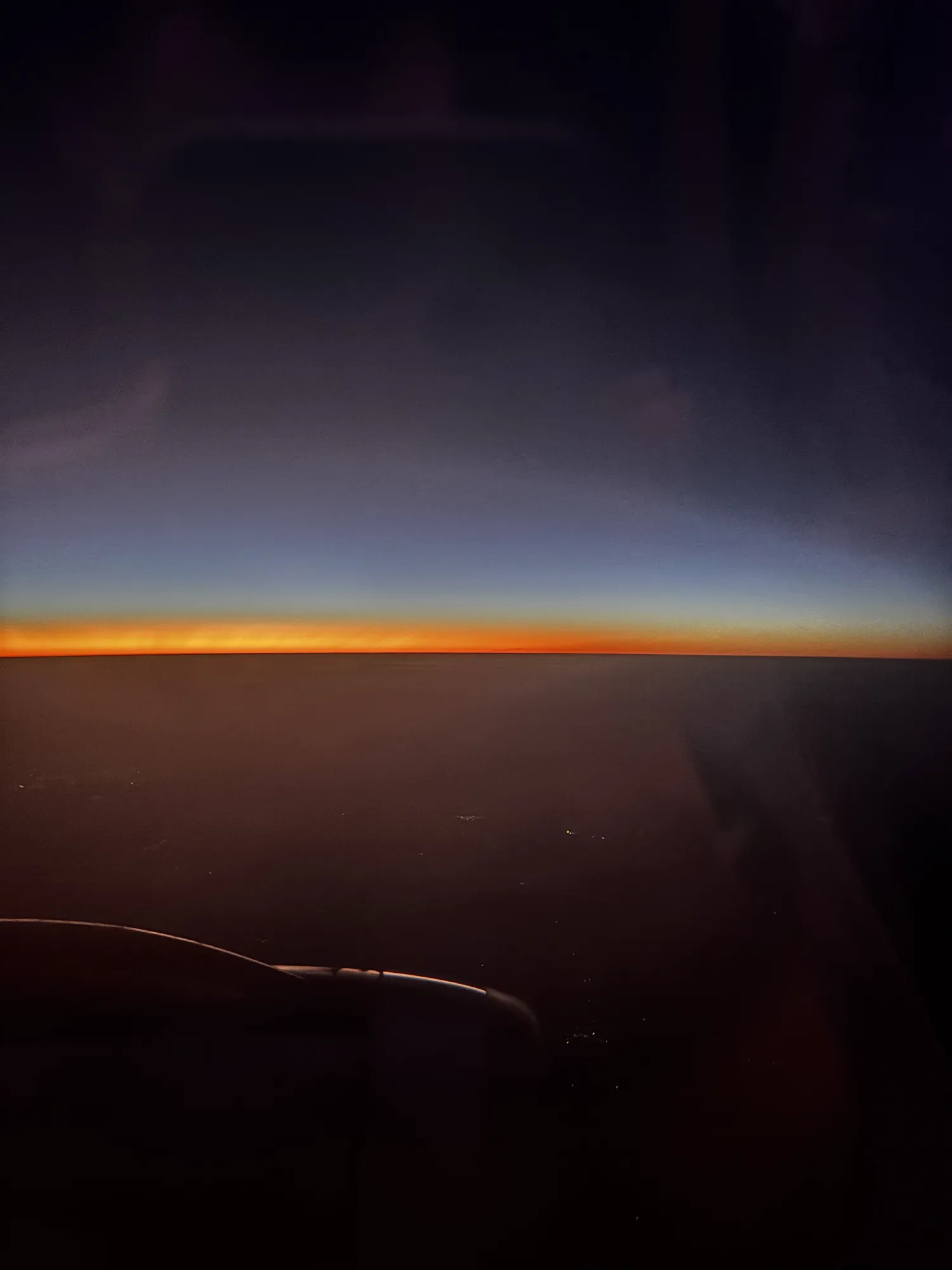 A thin orange line of sunrise on the horizon, seen from a plane window